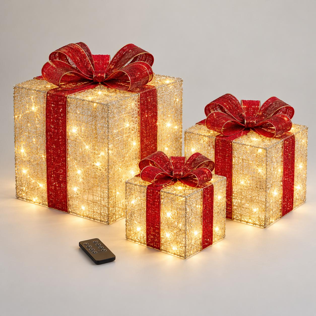 Three lighted Christmas gift boxes in nesting sizes with red ribbon bows and remote control